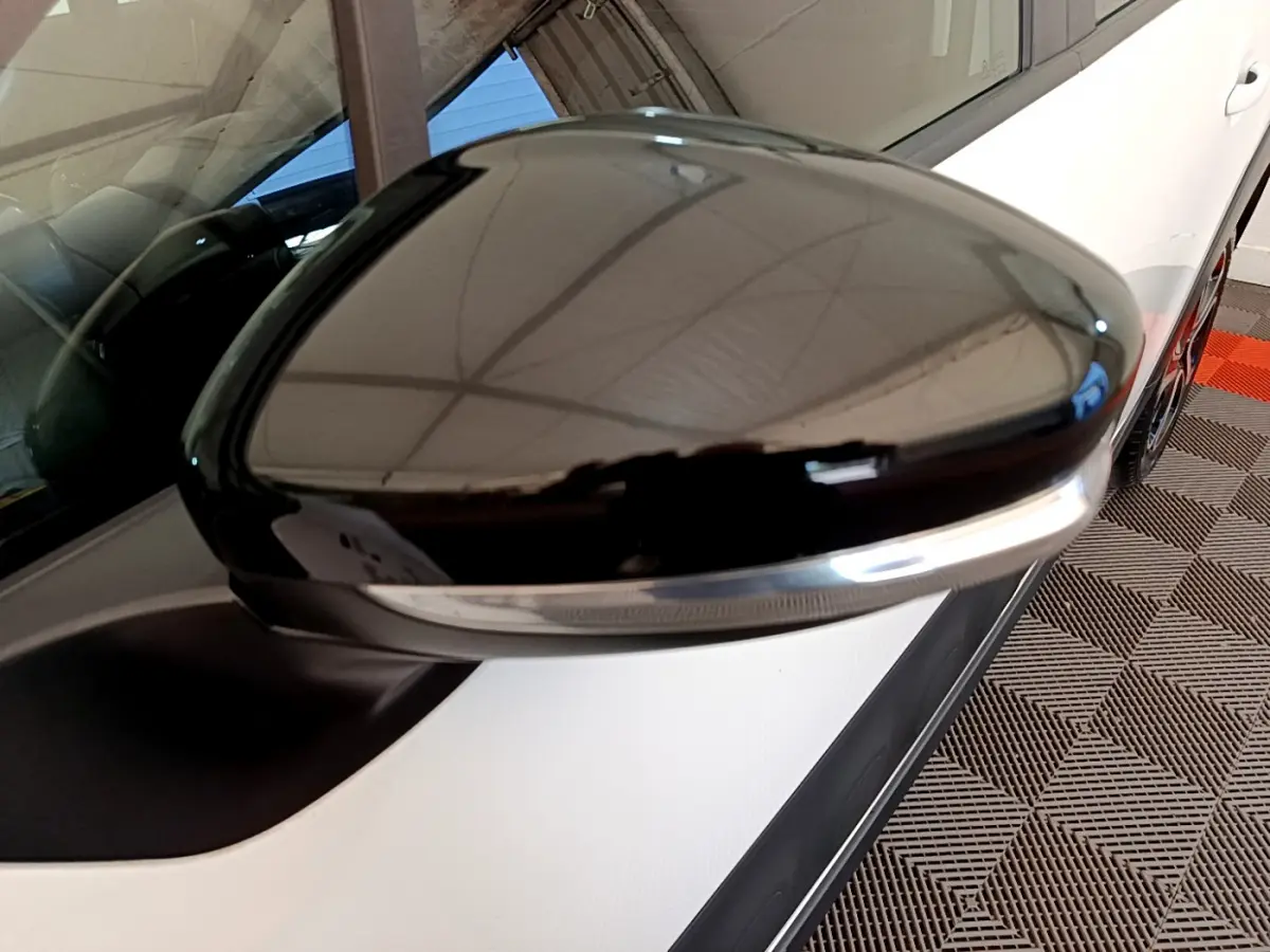 Rétroviseur noir brillant côté conducteur d'une Citroën C3 blanche vue en gros plan depuis l'avant gauche.