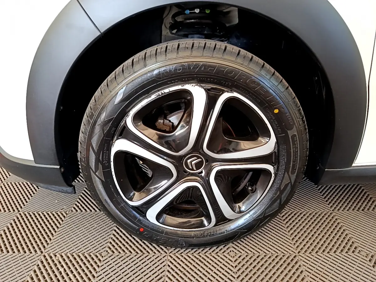Gros plan sur la roue arrière droite d'une Citroën C3 blanche avec passage de roue noir mat et jante en alliage.