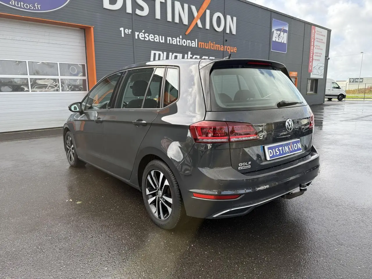 Volkswagen Golf Sportsvan gris Urano vue 3/4 arrière droit, avec jantes alliage et attelage visible.