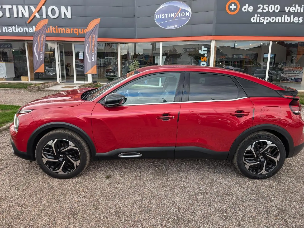 Profil côté gauche d'une Citroën C4 2024 rouge foncé avec jantes alliage et détails noirs mats sur bas de caisse.