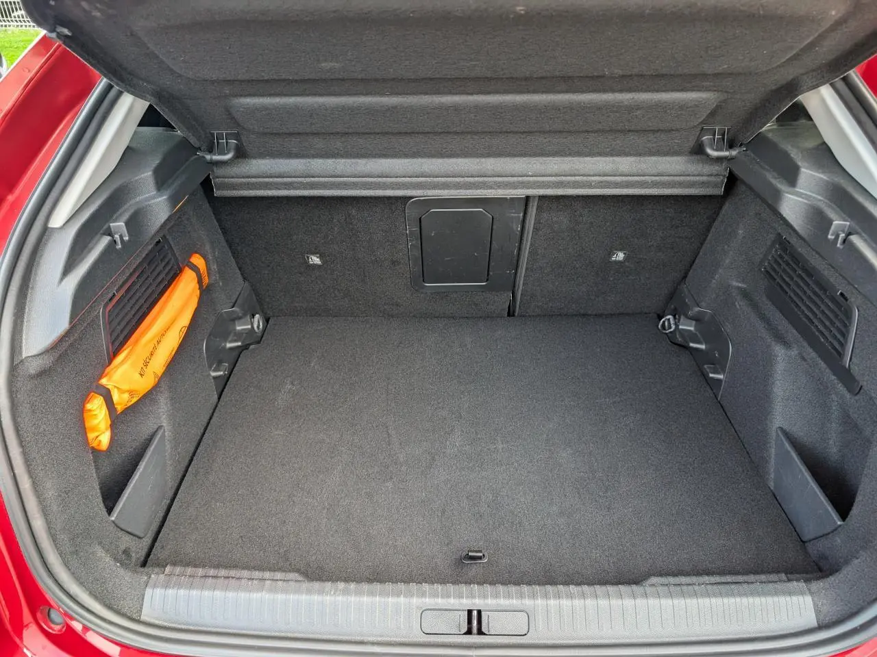 Coffre ouvert vu de l'arrière d'une Citroën C4 rouge foncé, espace de chargement propre et bien agencé.