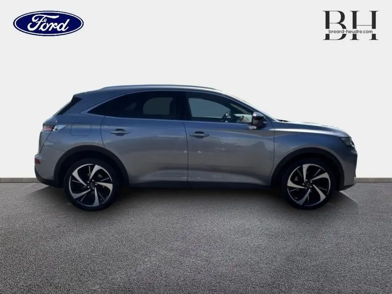 Vue de profil droit du SUV DS7 Crossback gris Artense avec jantes noires et argentées, sur fond neutre.