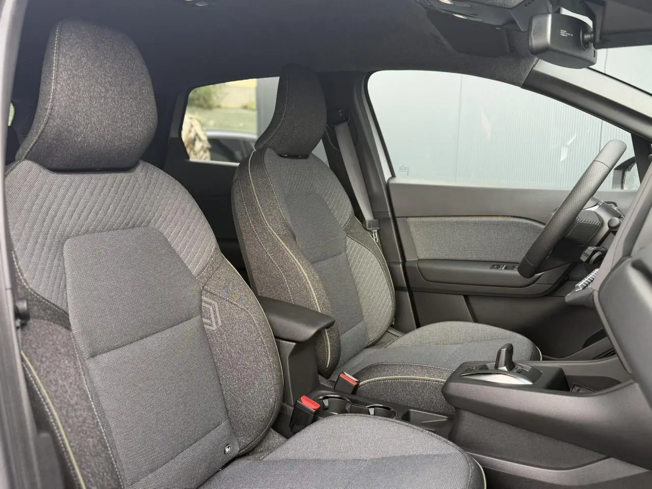 Vue intérieure côté droit du Renault Captur 2026, montrant les sièges tissu gris avec coutures contrastées et console centrale.