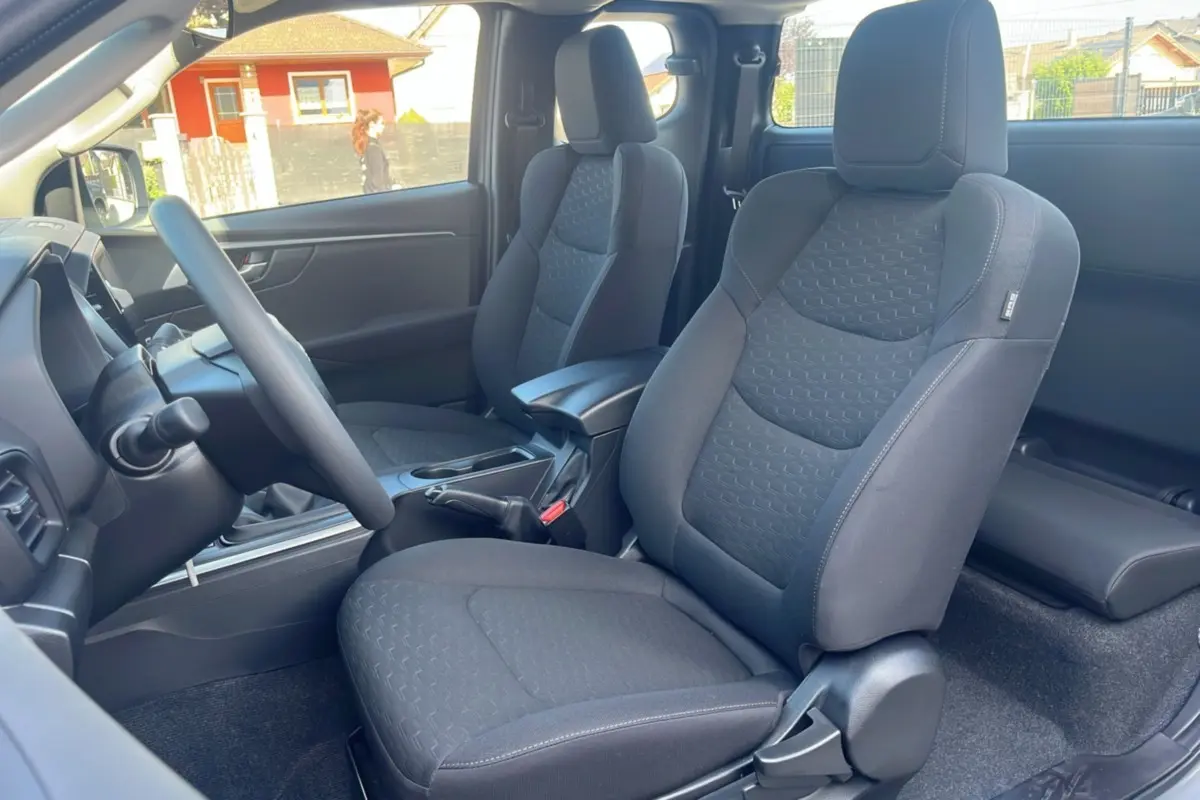 Vue intérieure côté conducteur de l'Isuzu D-MAX 2026, sièges tissu gris foncé avec accoudoir central avant.