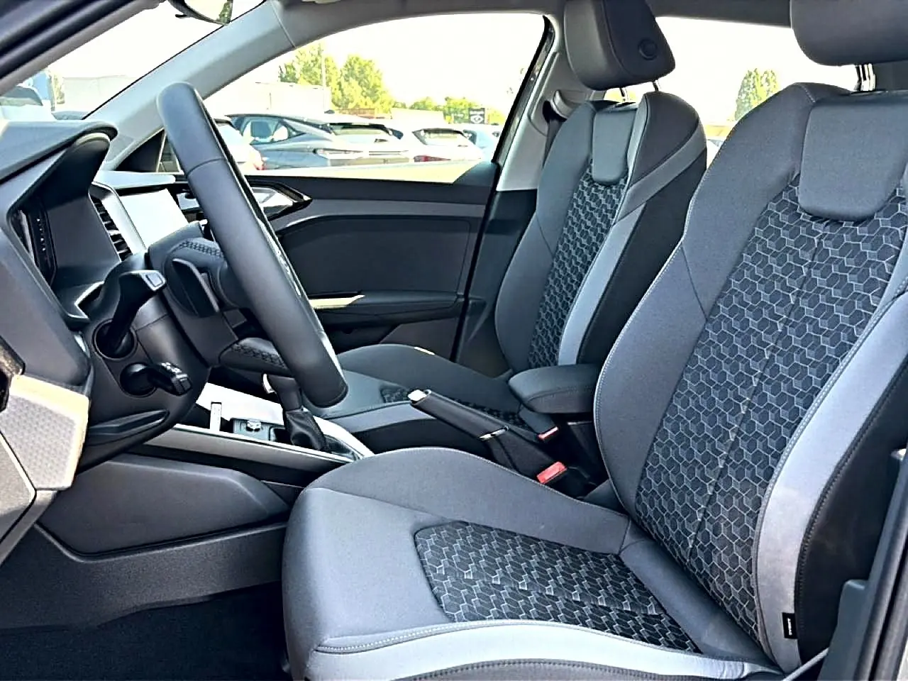 Vue intérieure côté gauche de l'Audi A1 Sportback 2026, sièges sport gris avec motifs hexagonaux et volant cuir multifonction.