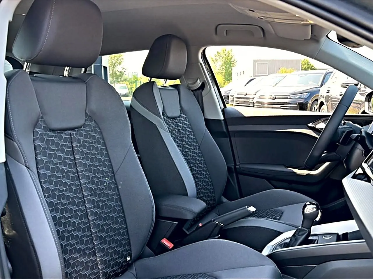 Vue intérieure avant de l’Audi A1 Sportback 30 TFSI 2026, sièges sport gris à motifs hexagonaux et accoudoir central.