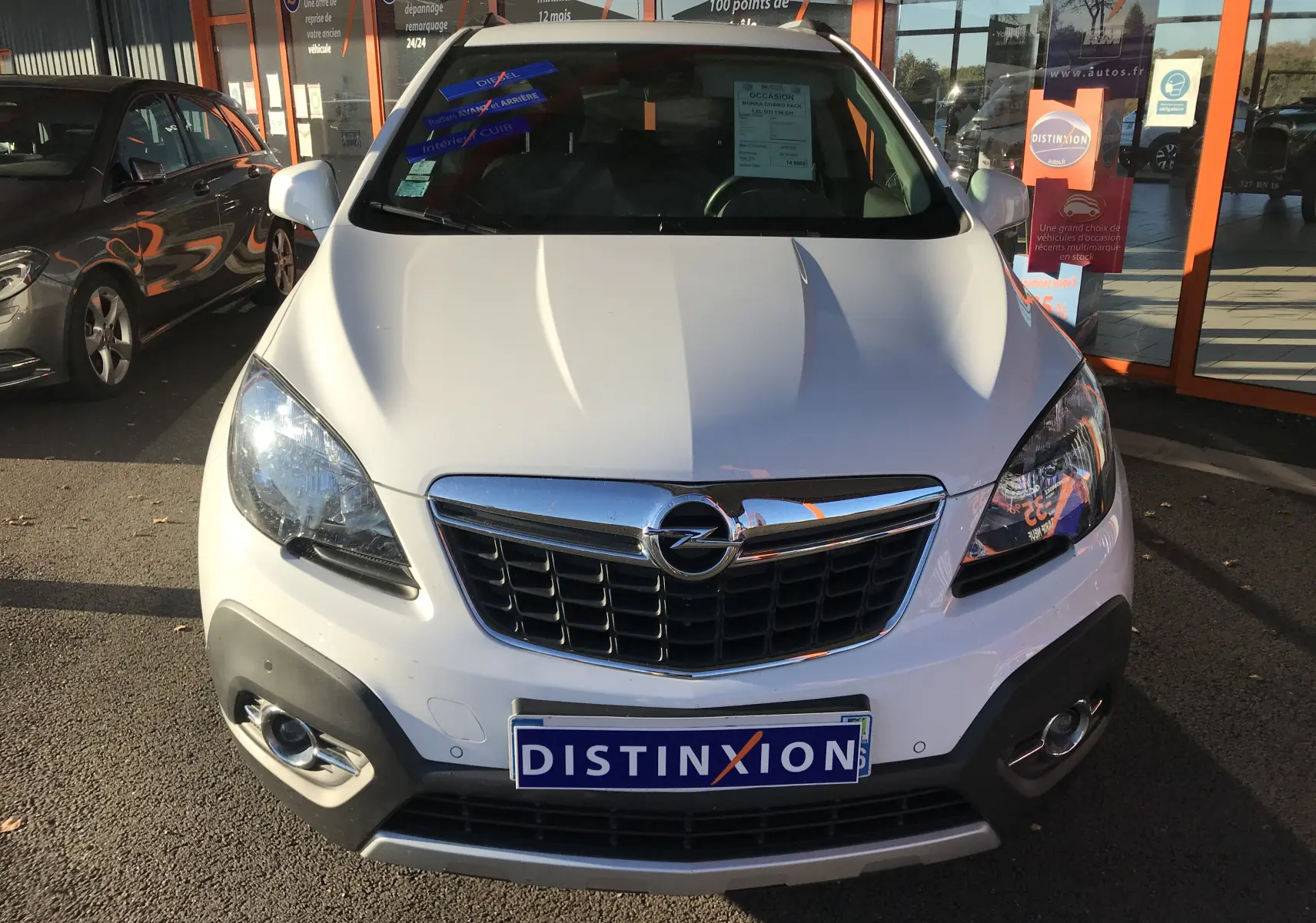 Vue frontale d'un Opel Mokka blanc 2015 avec calandre chromée et plaque "DISTINXION" visible en concession.