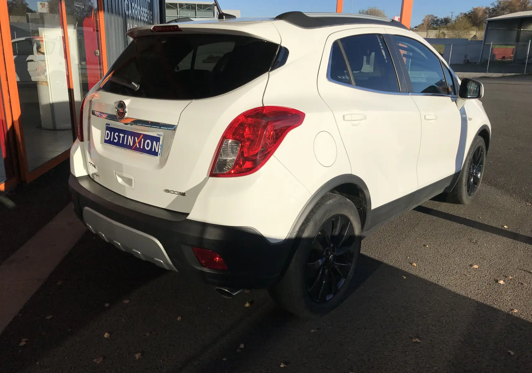 Vue 3/4 arrière droite d'un Opel Mokka blanc avec jantes noires et vitres teintées, stationné devant un bâtiment.