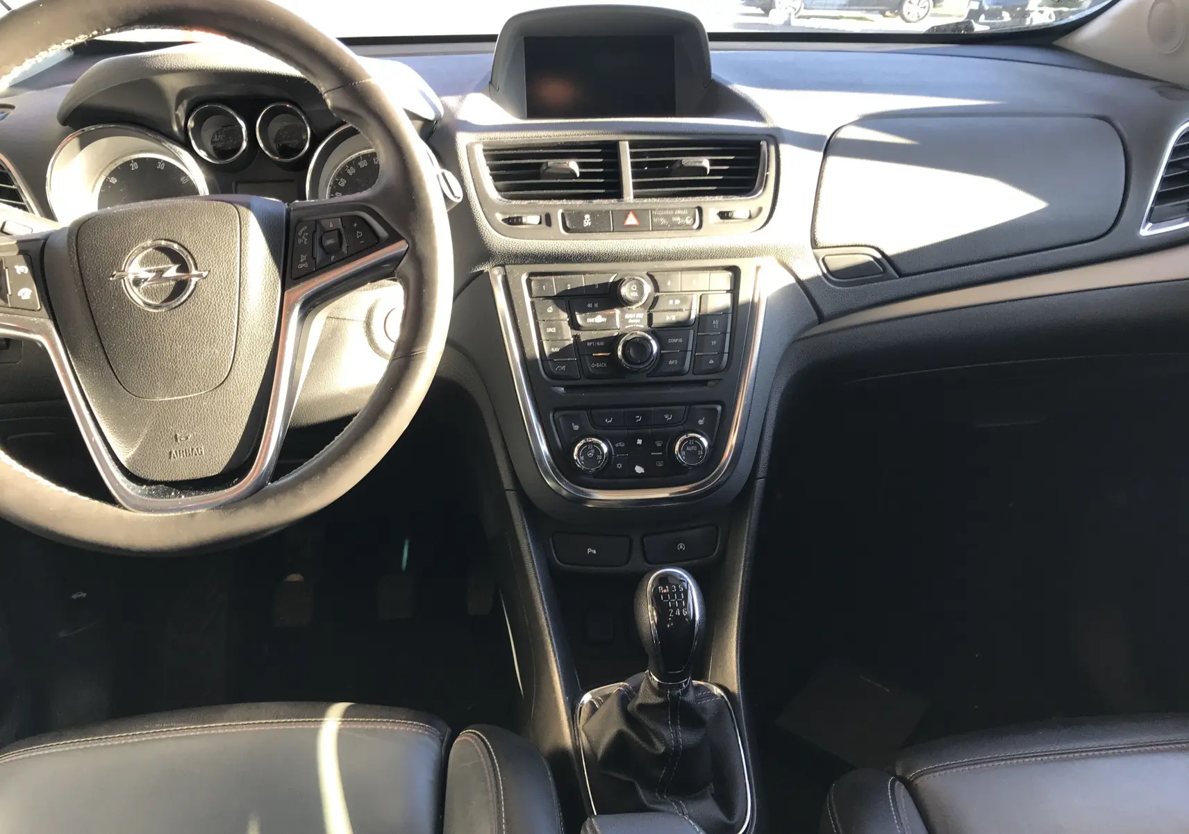 Intérieur noir de l'Opel Mokka 2015, vue du tableau de bord et volant avec boîte manuelle au centre.