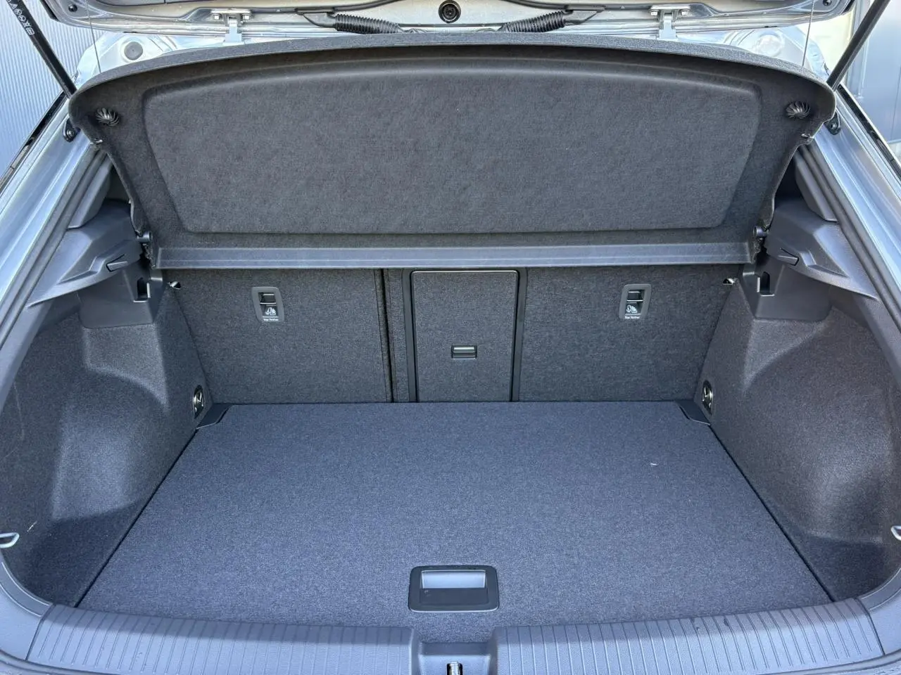 Coffre ouvert vu de l'arrière du Volkswagen T-Roc gris Pyrite, montrant un espace de chargement propre et bien agencé.