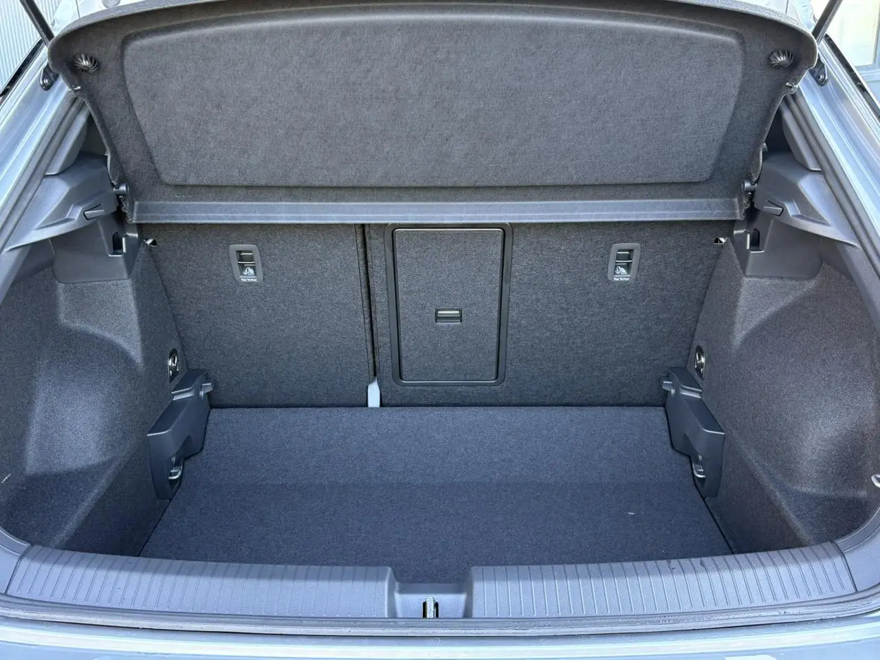 Coffre ouvert du Volkswagen T-Roc gris pyrite, vue arrière montrant l'espace de chargement et la trappe centrale.