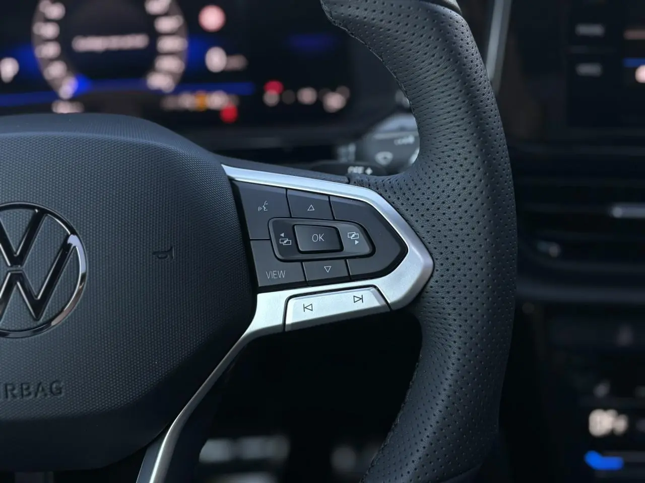 Gros plan sur le volant en cuir perforé du Volkswagen T-Roc 2025 avec commandes multifonctions et logo VW central.