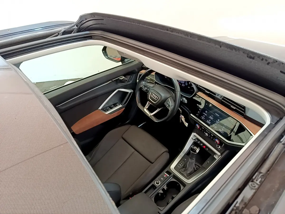 Vue intérieure côté conducteur de l'Audi Q3 35 TDI bleu, montrant le volant cuir et la console centrale moderne.