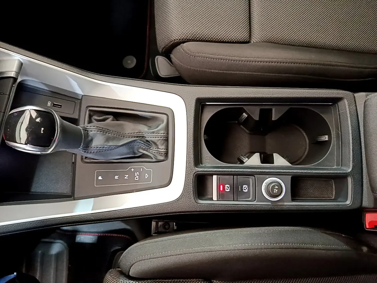 Vue plongeante sur la console centrale noire de l'Audi Q3 35 TDI 150 S tronic avec levier de vitesse et porte-gobelets.