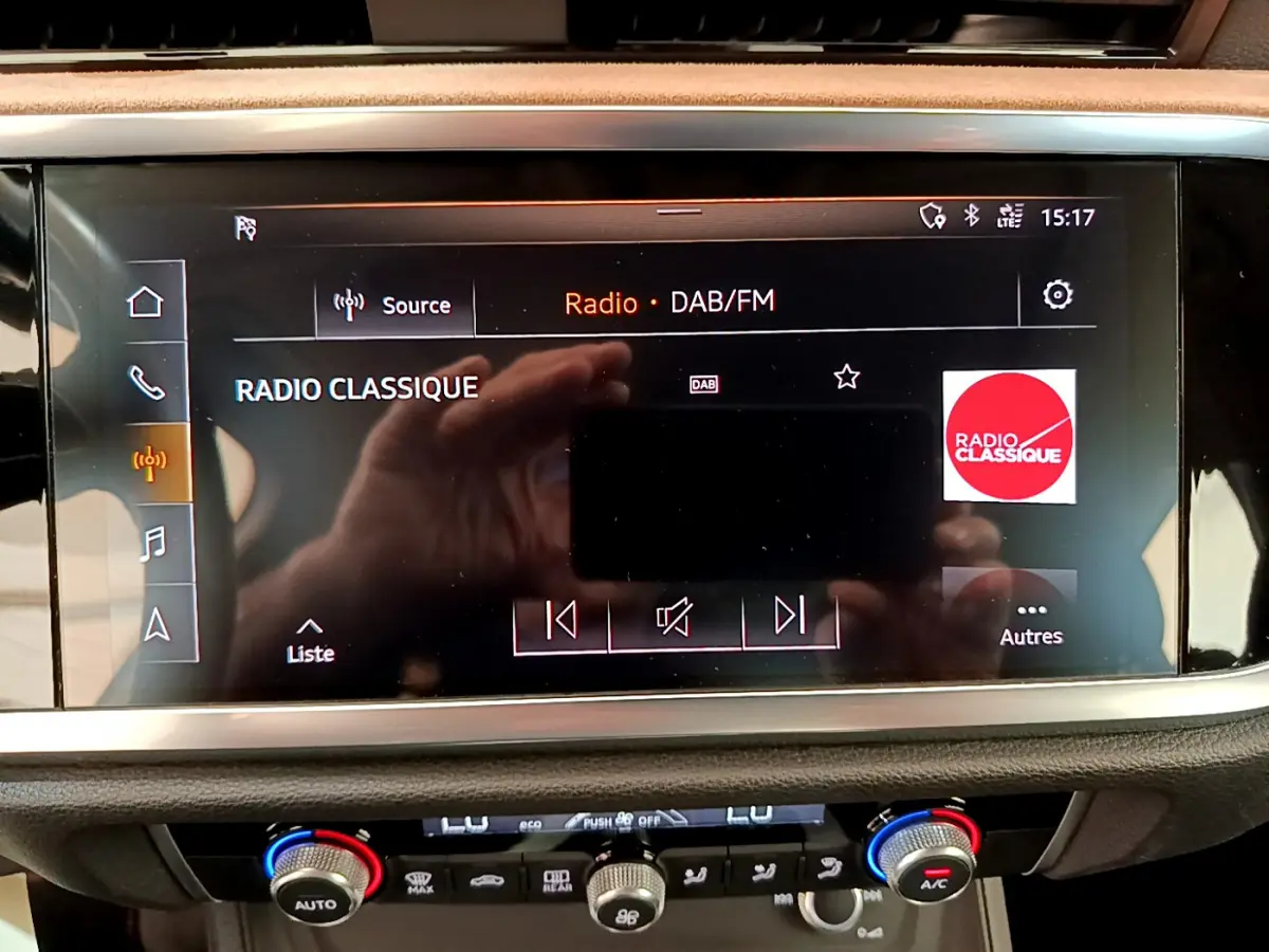 Écran tactile central affichant la radio DAB/FM sur Audi Q3 bleu, avec commandes climatisation en dessous.