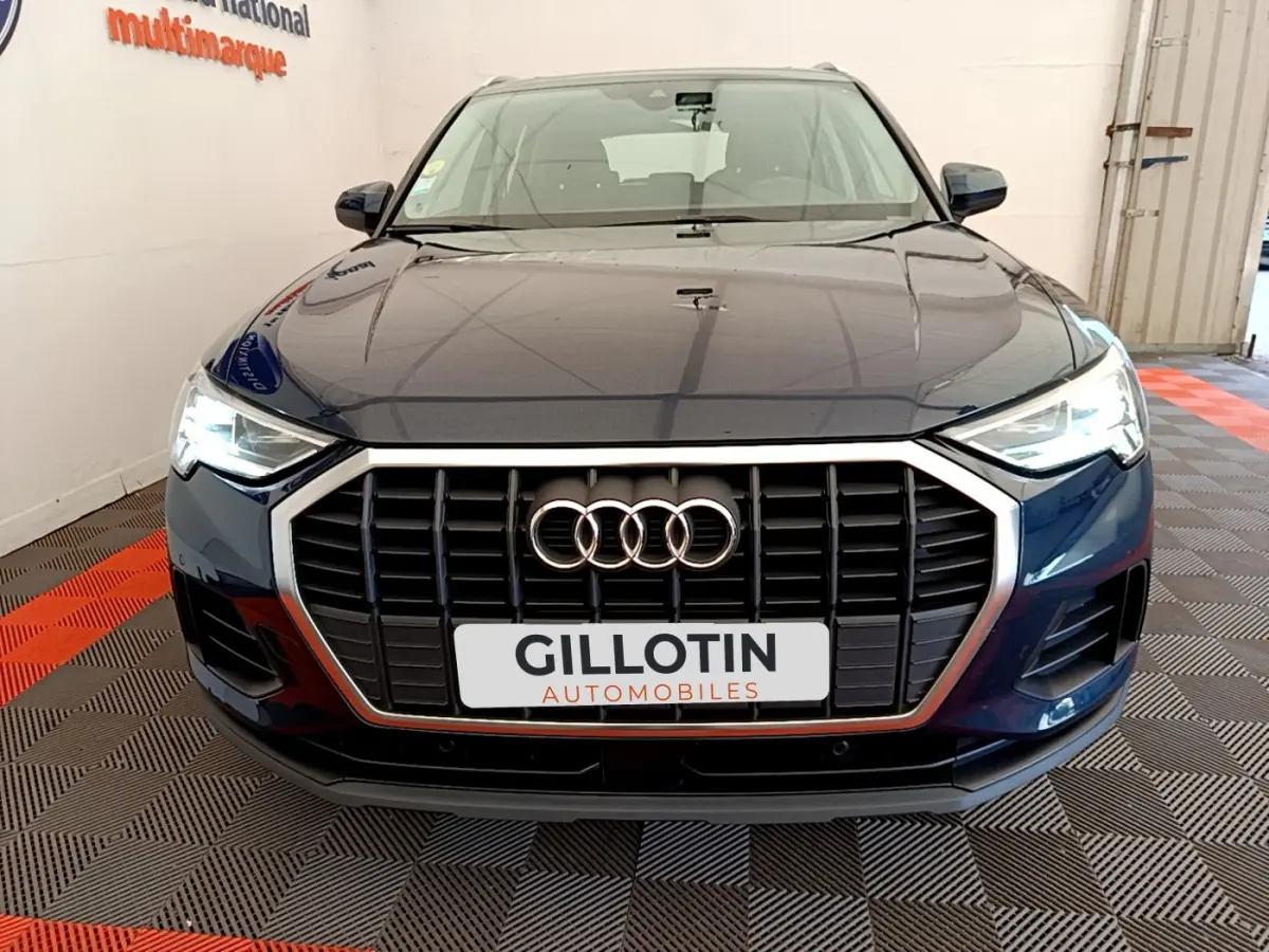 Vue frontale d'un Audi Q3 bleu 2020 avec calandre noire et phares LED allumés dans un showroom.