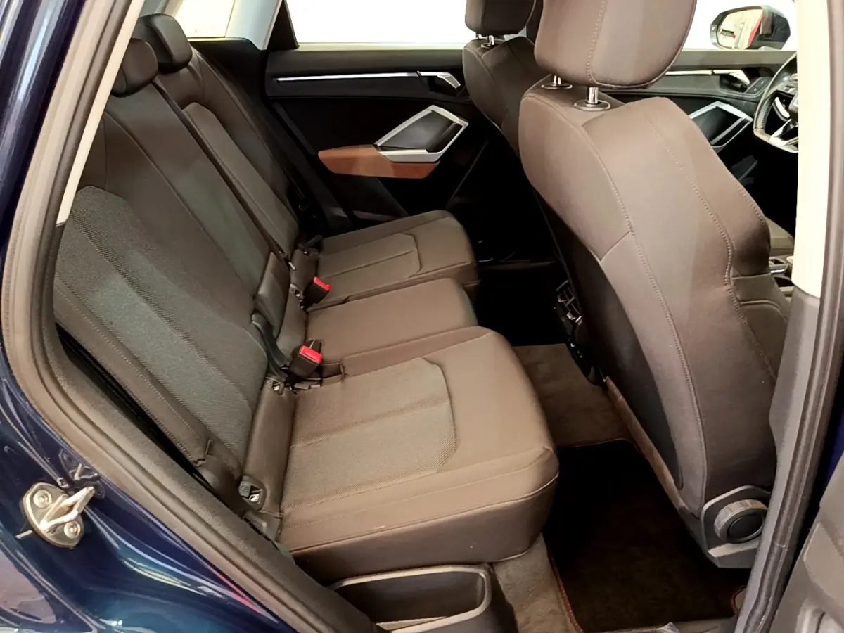 Vue intérieure côté arrière gauche de l'Audi Q3 bleu 35 TDI, montrant la banquette arrière en tissu gris foncé.