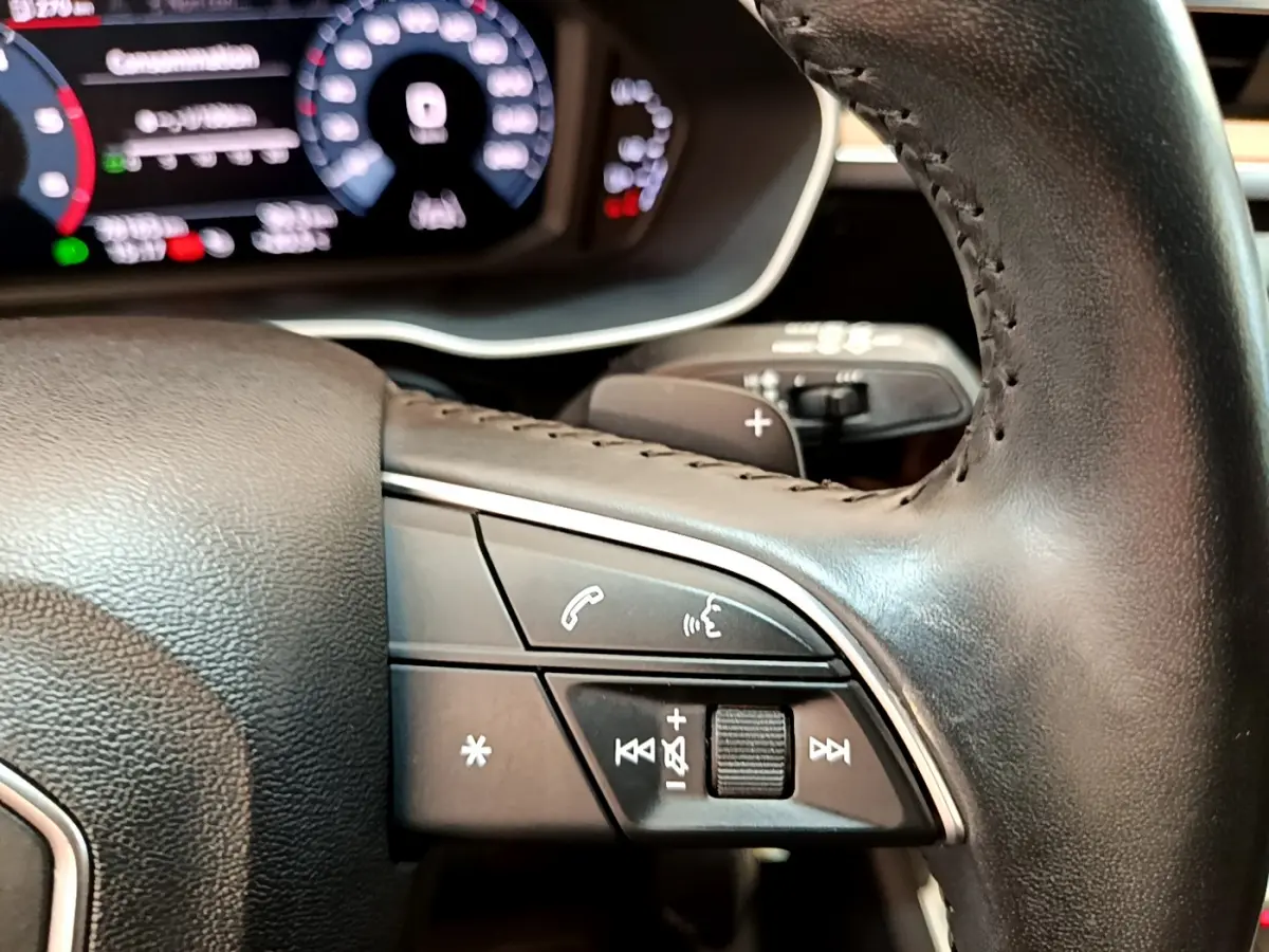 Gros plan sur les commandes multifonctions du volant cuir noir de l'Audi Q3 35 TDI 2020 avec tableau de bord numérique.