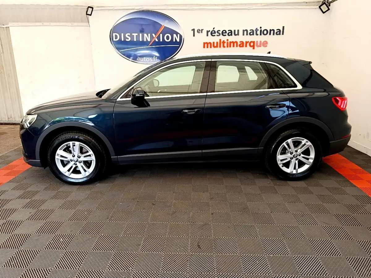 Audi Q3 bleu 2020 vue de profil côté gauche, avec jantes alliage et feux arrière LED visibles en intérieur showroom.