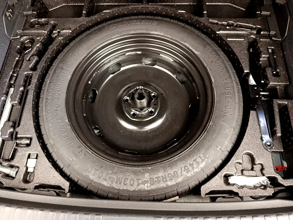 Gros plan sur la roue de secours noire dans le coffre de l'Audi Q3 bleu 35 TDI 2020, entourée des outils de bord.