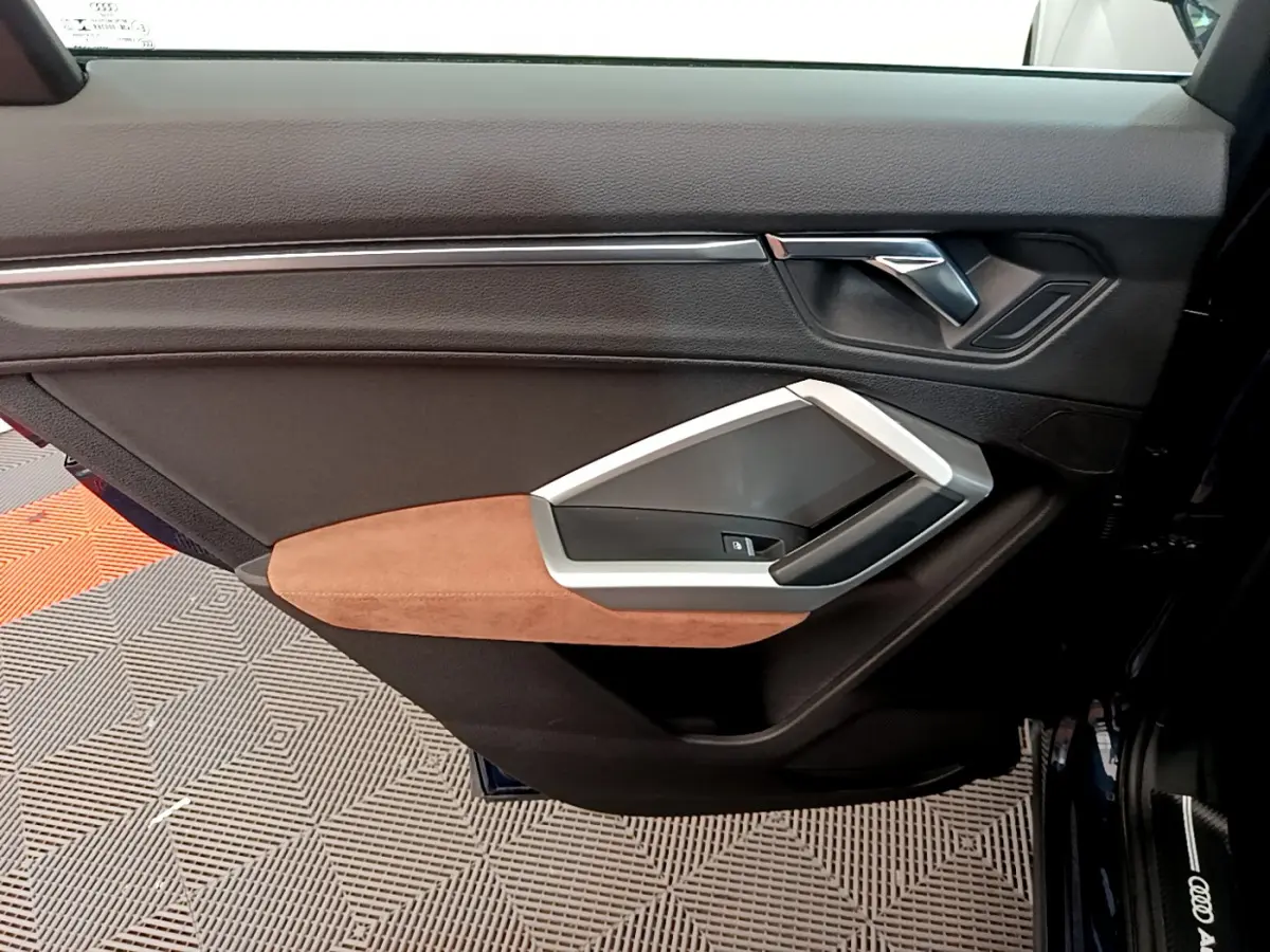 Gros plan sur la porte avant gauche de l'Audi Q3 bleu 2020, avec garniture noire et accoudoir marron clair en alcantara.