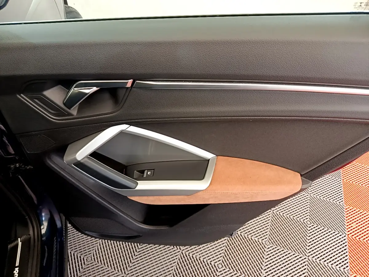 Gros plan sur la garniture intérieure côté gauche de la porte d'un Audi Q3 bleu avec accoudoir beige et insert argenté.