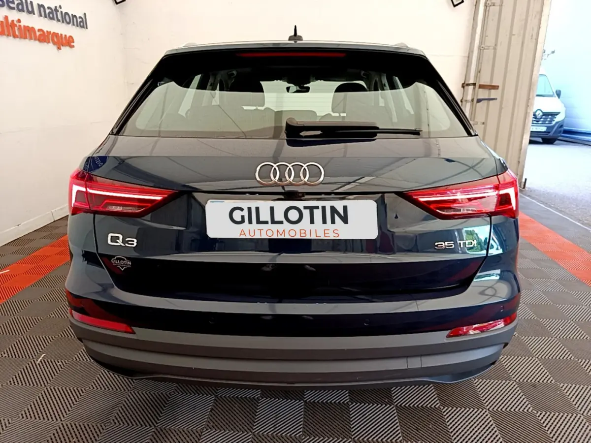 Vue arrière d'un Audi Q3 bleu 35 TDI avec feux LED et logo distinctif sur un sol damier intérieur.