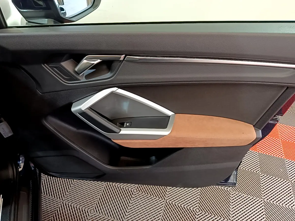 Gros plan sur la porte côté gauche de l'Audi Q3 bleu, avec garniture marron et poignée argentée moderne.
