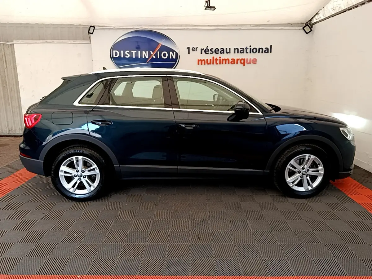 Audi Q3 bleu foncé vu de profil côté gauche, avec jantes alliage et feux arrière LED visibles en intérieur showroom.