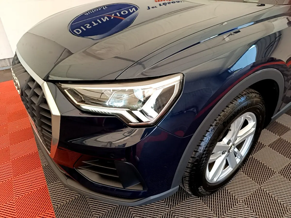 Vue 3/4 avant droit d'un Audi Q3 bleu foncé mettant en valeur son phare LED distinctif et sa calandre hexagonale.
