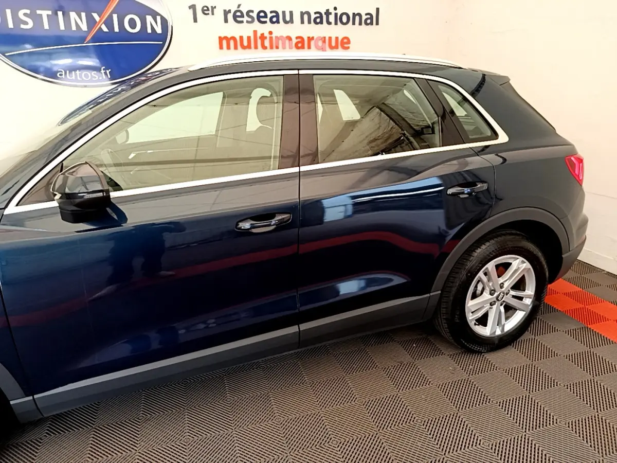 Profil côté gauche d'un Audi Q3 bleu 2020 avec jantes alliage et rétroviseurs noirs en intérieur showroom.