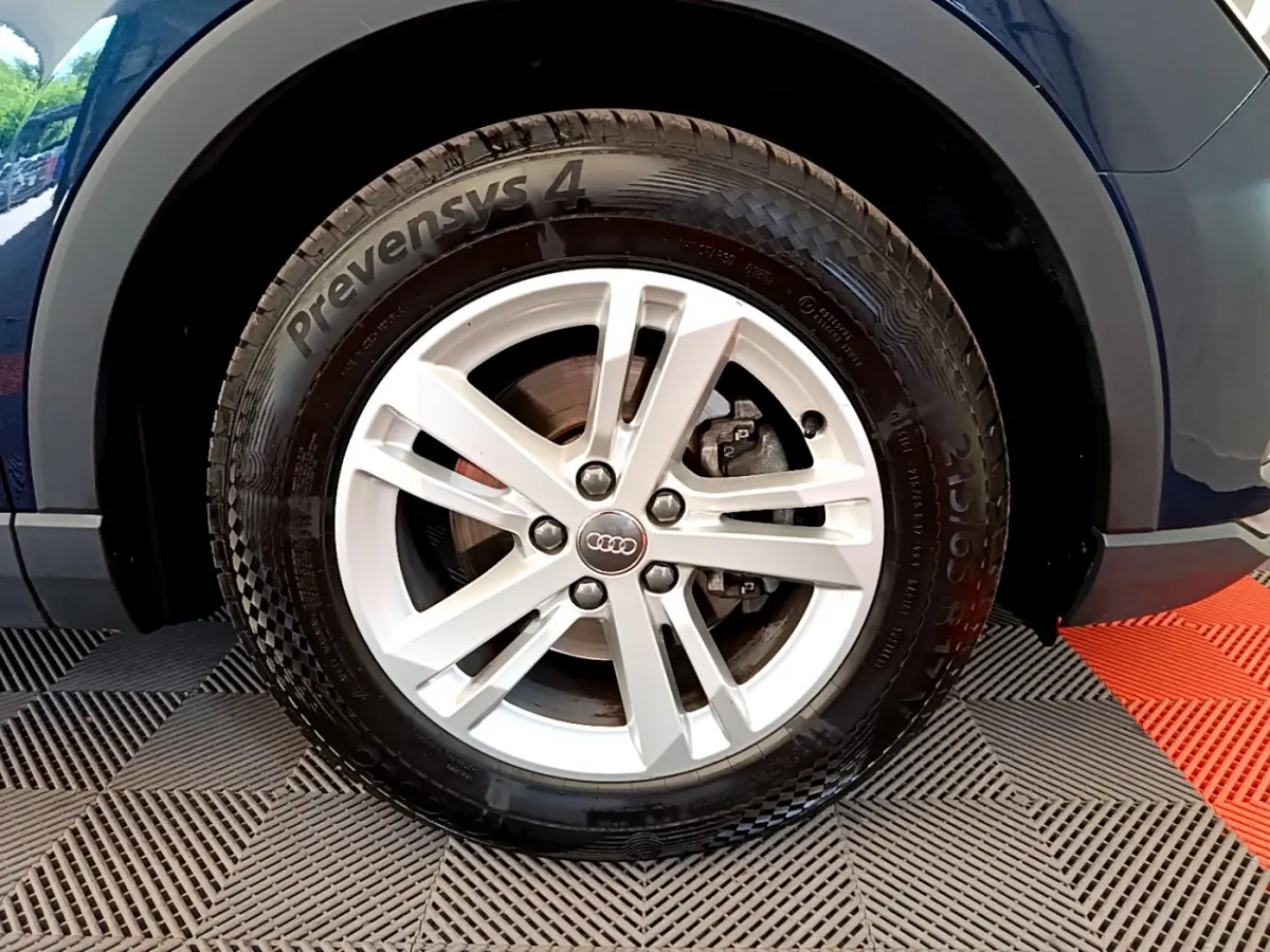Gros plan sur la roue avant gauche d'un Audi Q3 bleu 35 TDI 150 S tronic avec jante argentée à 5 branches.