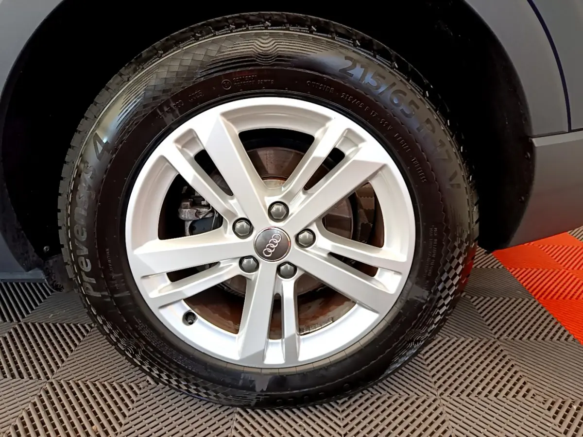 Gros plan sur la roue avant droite d'un Audi Q3 bleu 2020, mettant en valeur la jante argentée à cinq branches.