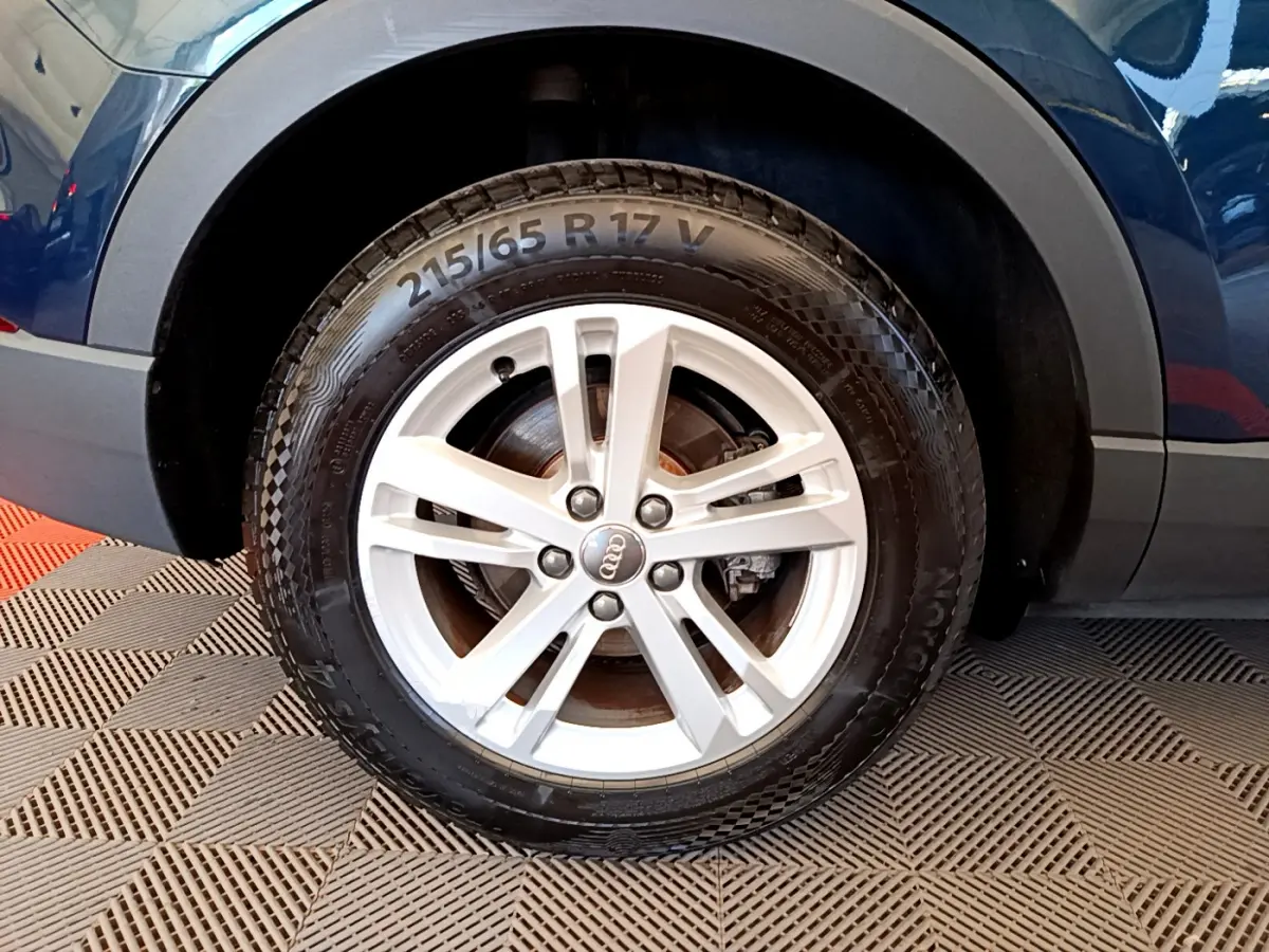 Gros plan sur la roue avant gauche d’un Audi Q3 bleu 2020 avec jante alliage argentée et pneu 215/65 R17.