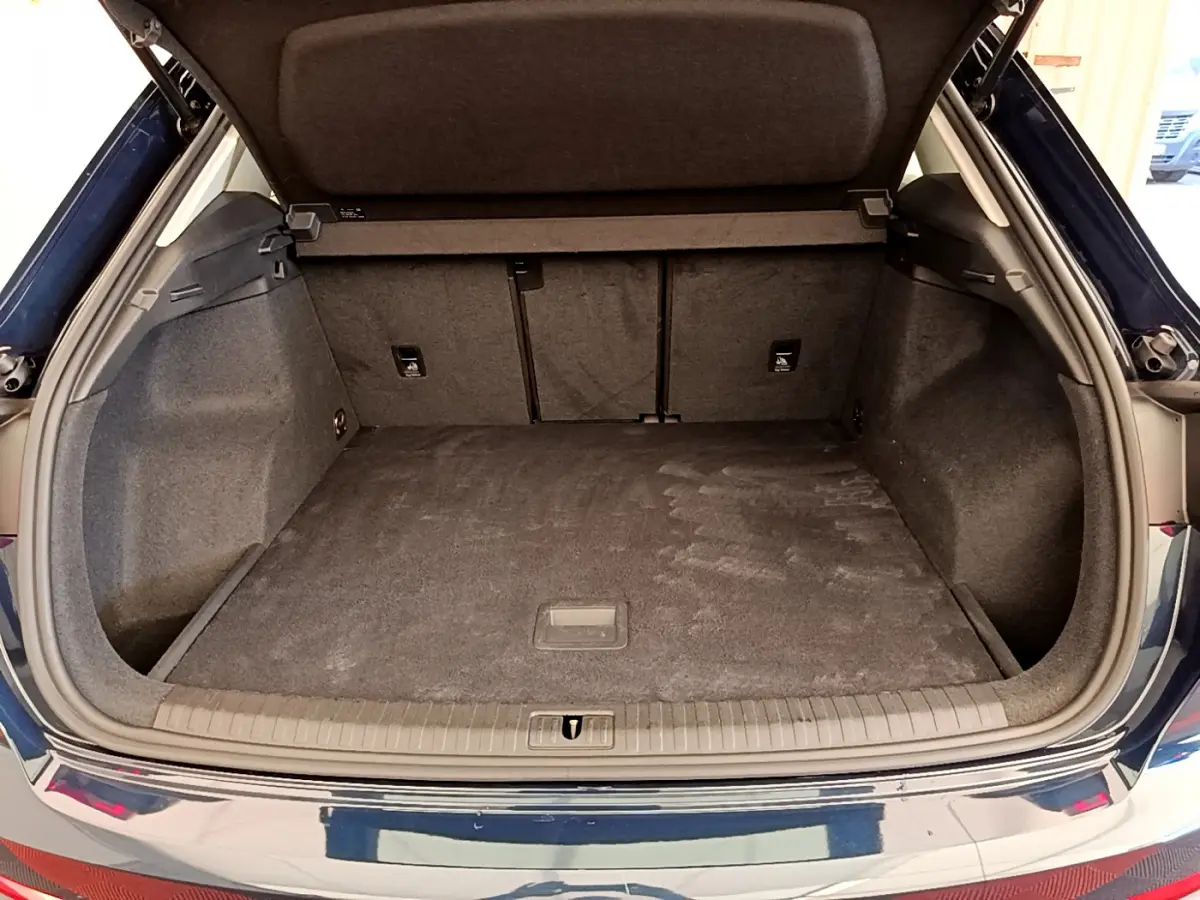 Coffre ouvert de l'Audi Q3 bleu 2020, vue arrière montrant l'espace de chargement vide et tapis gris.