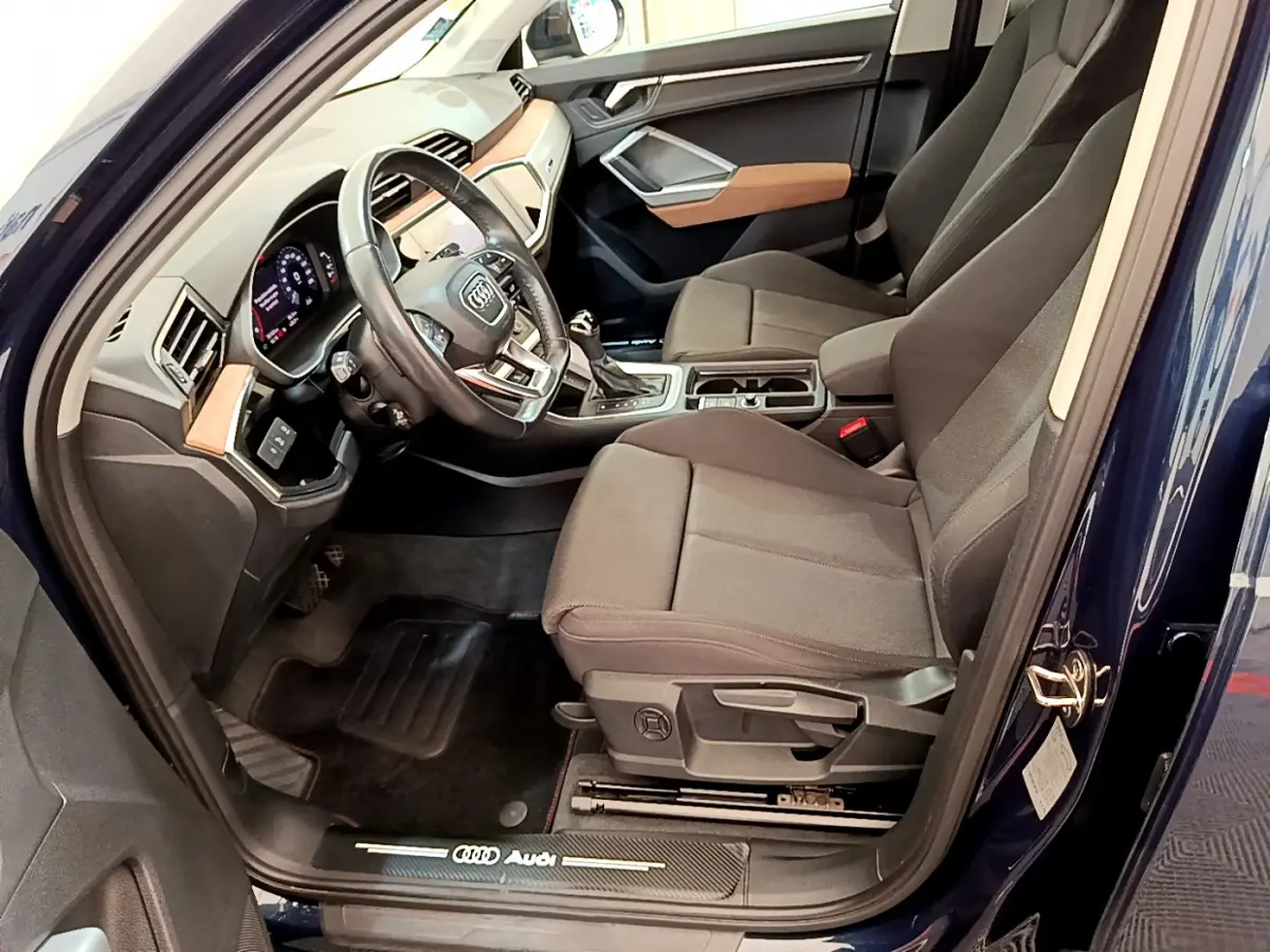 Intérieur côté conducteur d’un Audi Q3 bleu 2020, avec sièges tissu gris et tableau de bord moderne.