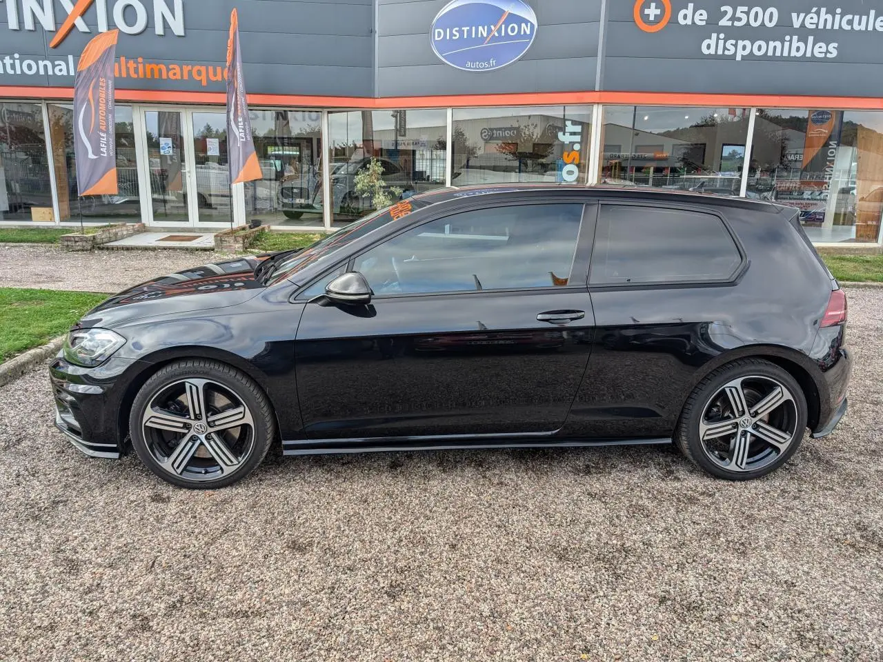 Profil côté gauche d'une Volkswagen Golf noire 2017 avec jantes alliage et vitres arrière teintées devant un showroom