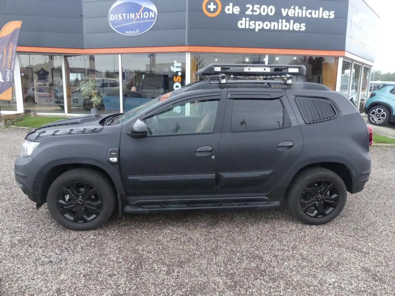 Profil côté gauche d'un Dacia Duster noir 2023 avec galerie de toit, marchepied et jantes alliage noires.