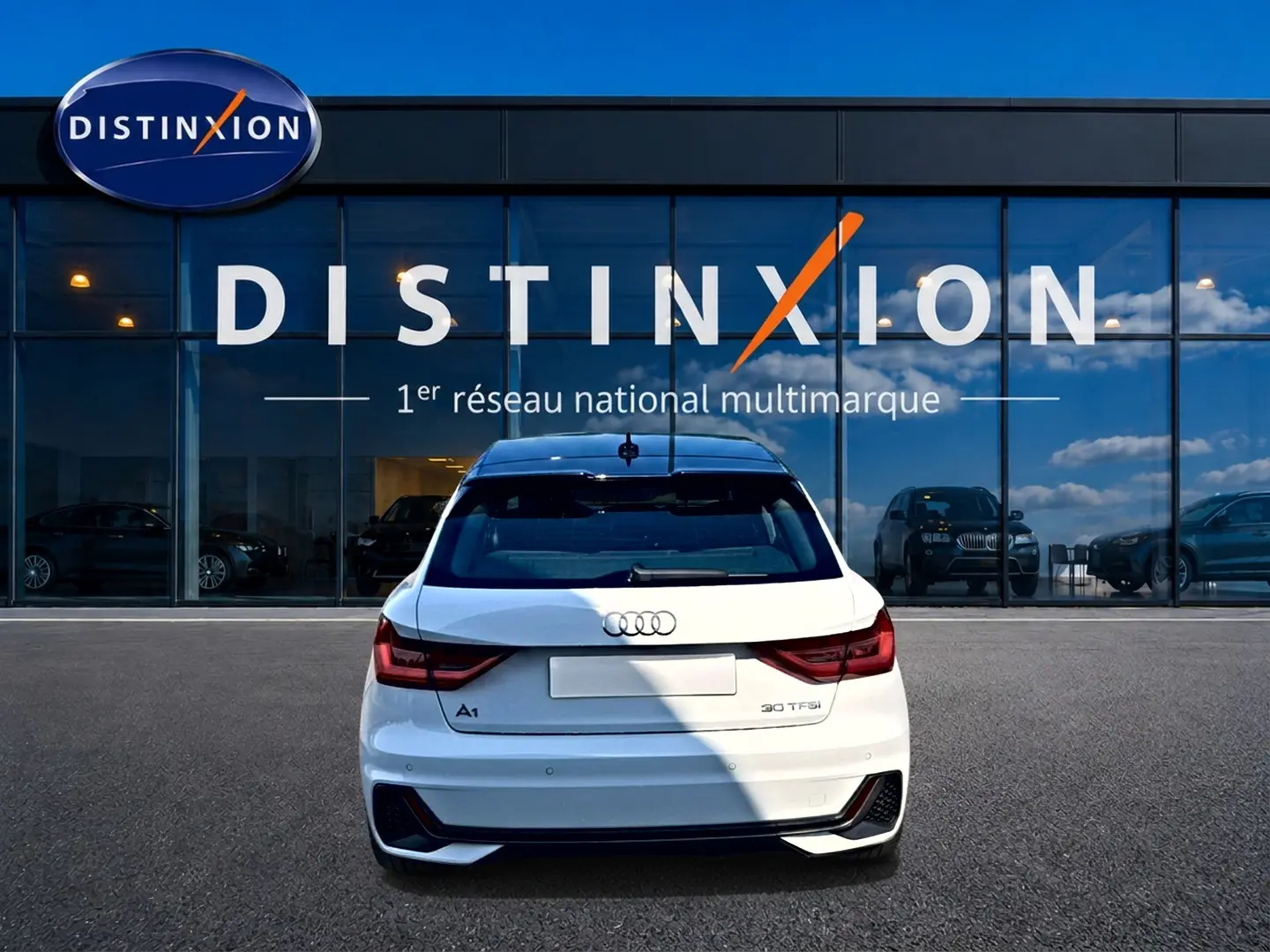 Vue arrière d'une Audi A1 Sportback blanche avec toit noir, feux LED et logo distinctif sur fond de vitrine Distinxion.