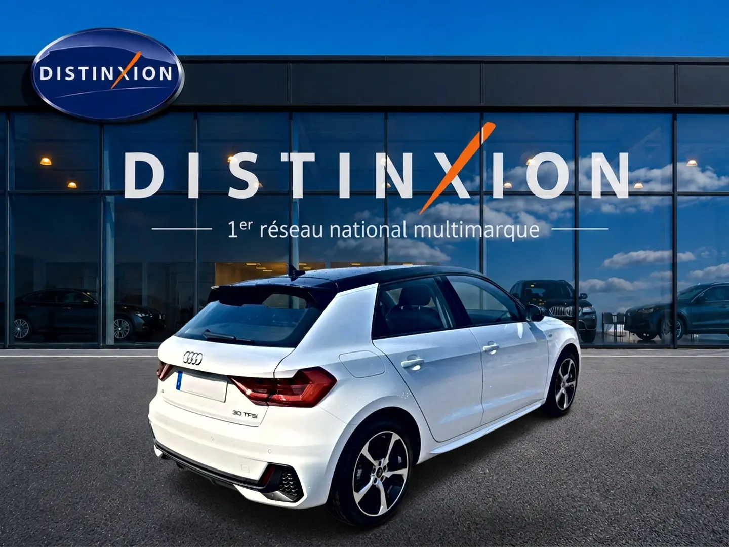 Audi A1 Sportback blanc toit noir en 3/4 arrière droit, avec jantes alu et becquet arrière visible devant showroom Distinxion.