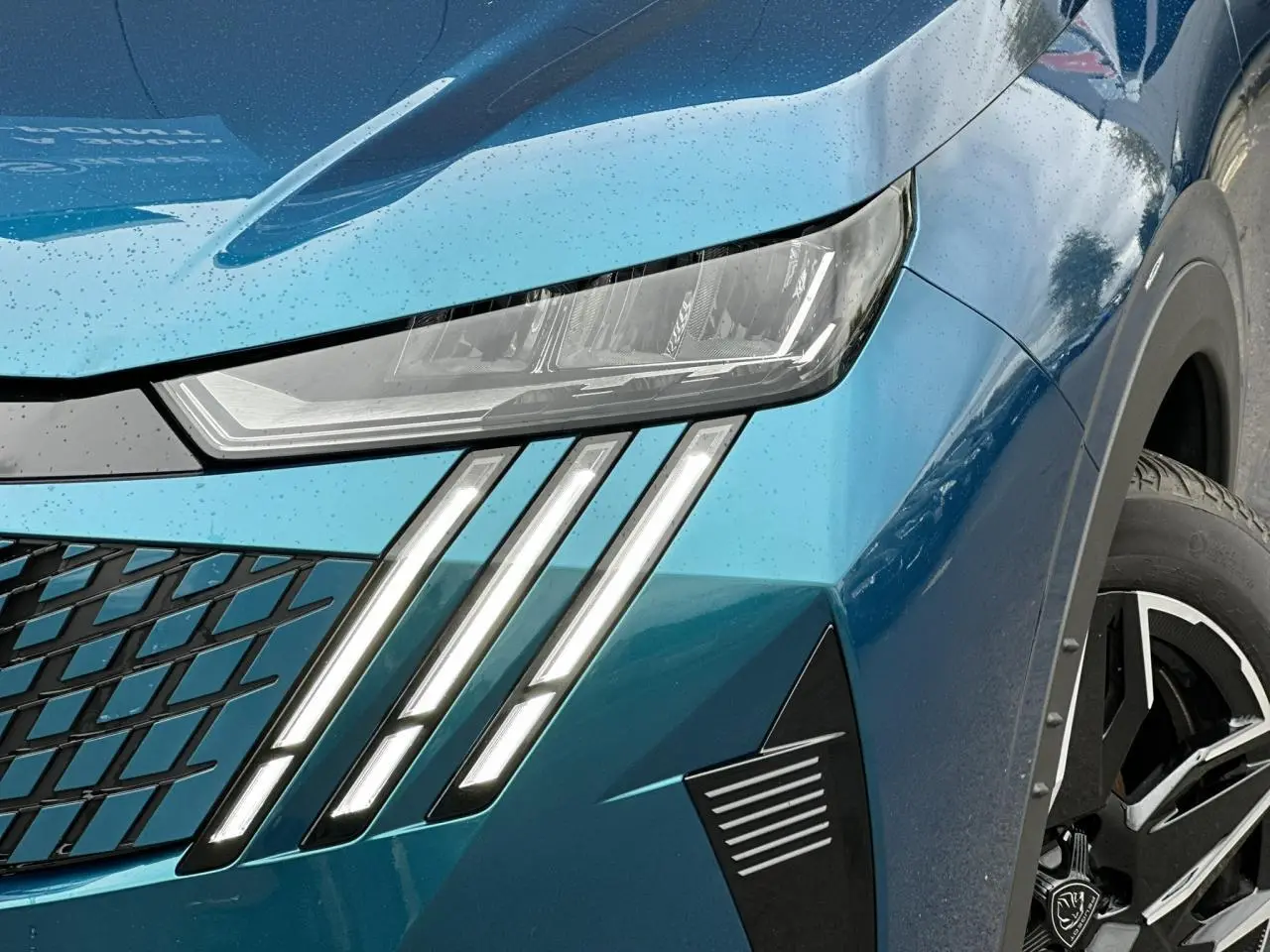 Gros plan sur le phare avant gauche et la calandre du Peugeot 3008 Hybrid bleu Obsession avec jante alliage 19 pouces.