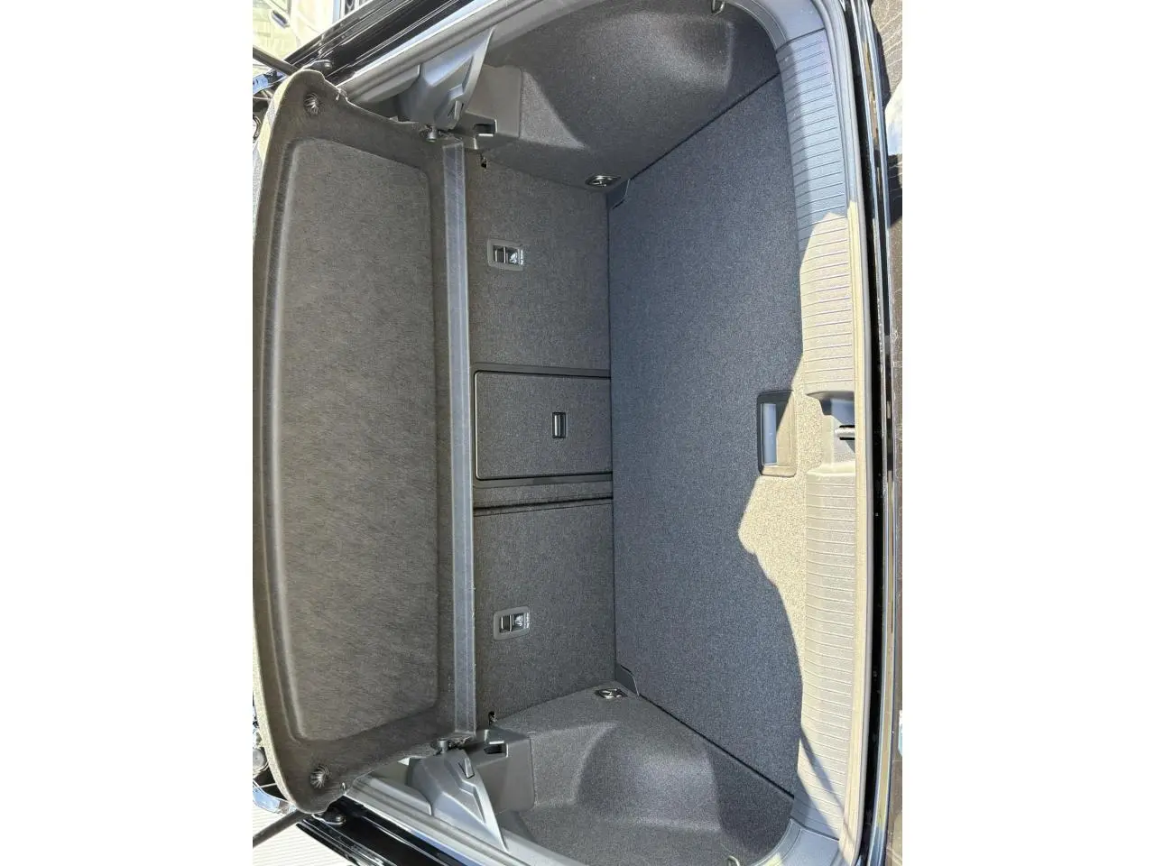 Coffre ouvert du Volkswagen T-Roc noir Grenadilla, montrant l'espace de rangement et la finition intérieure grise.