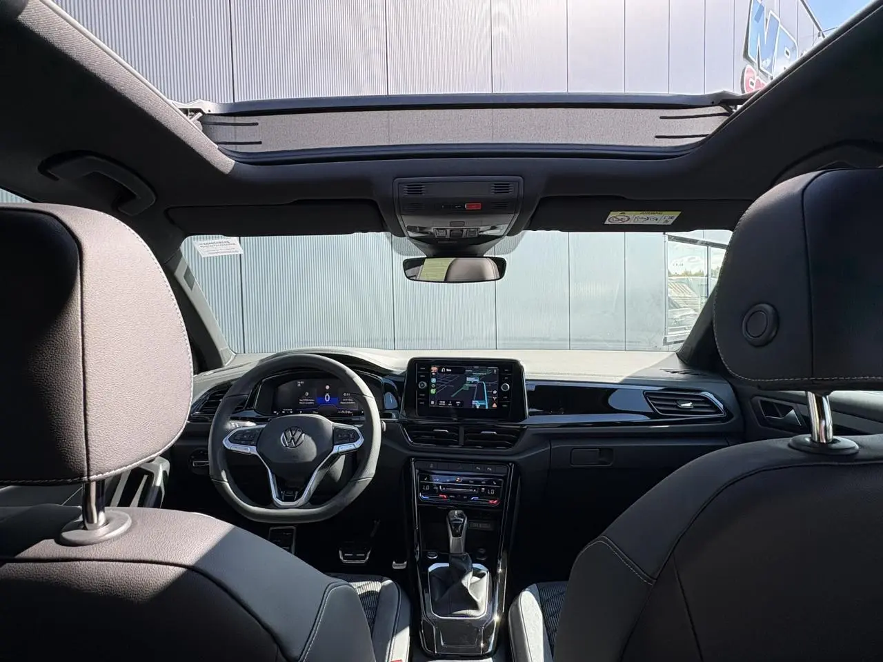 Intérieur noir du Volkswagen T-Roc 2025 vu de l'arrière, avec toit ouvrant en verre et tableau de bord digital.