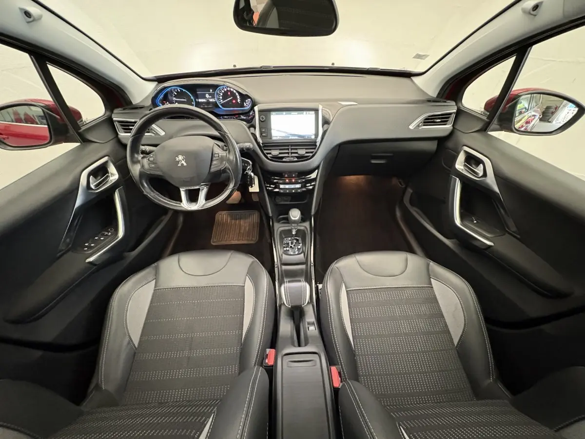 Vue intérieure avant de la Peugeot 2008 rouge, montrant le tableau de bord, volant cuir et sièges noirs.