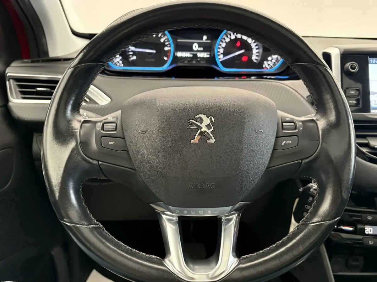 Vue rapprochée du volant cuir noir de la Peugeot 2008 rouge avec tableau de bord digital et commandes intégrées.