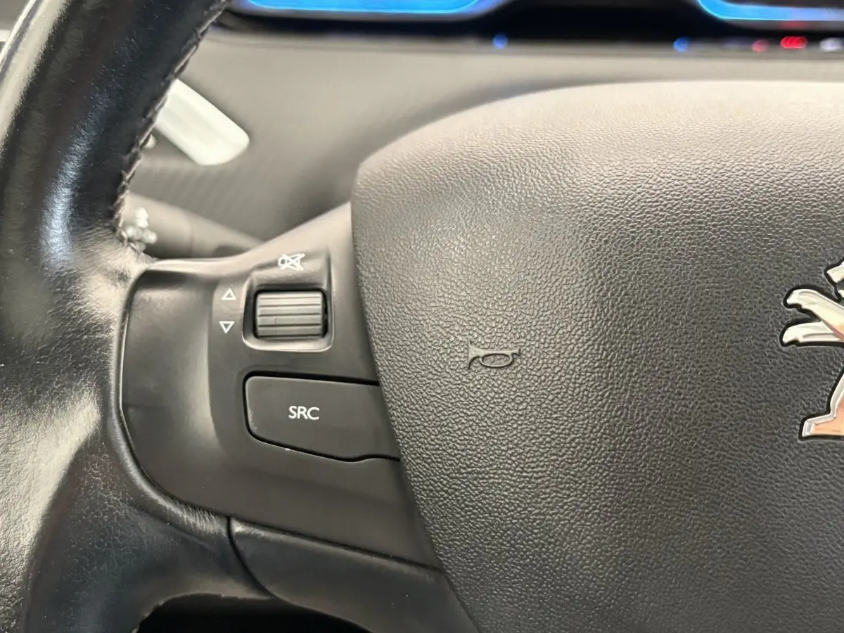 Gros plan sur le volant cuir noir du Peugeot 2008 avec commandes audio intégrées et logo lion central.