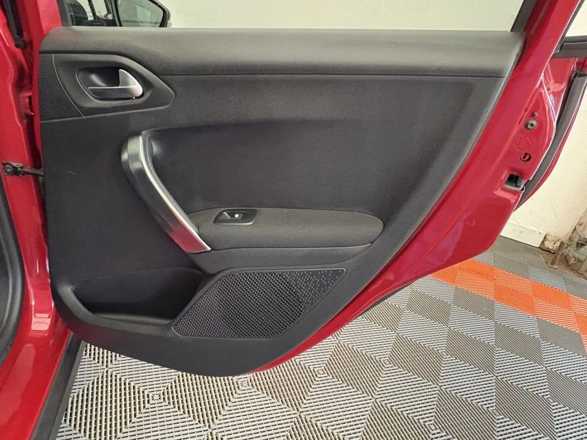 Porte arrière gauche ouverte d'une Peugeot 2008 rouge, montrant le panneau intérieur noir avec poignée chromée.
