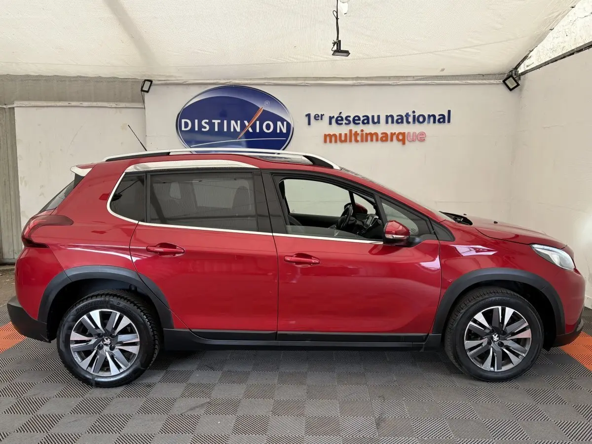 Profil droit d'un Peugeot 2008 rouge 2019 avec jantes alliage et barres de toit chromées en showroom.