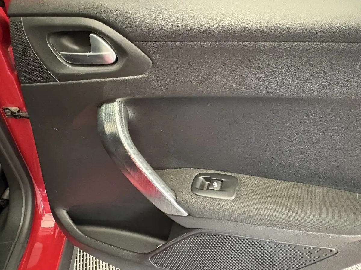 Gros plan sur la porte avant gauche rouge d'une Peugeot 2008 avec poignée argentée et commande de lève-vitre.