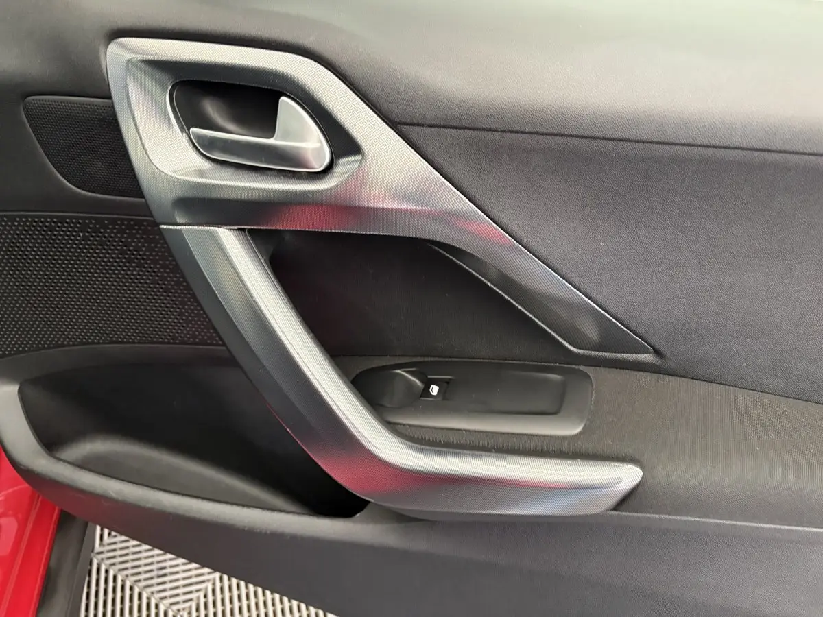 Poignée intérieure côté gauche de la porte rouge d'un Peugeot 2008 Puretech 110 Allure, avec insert gris métallique.